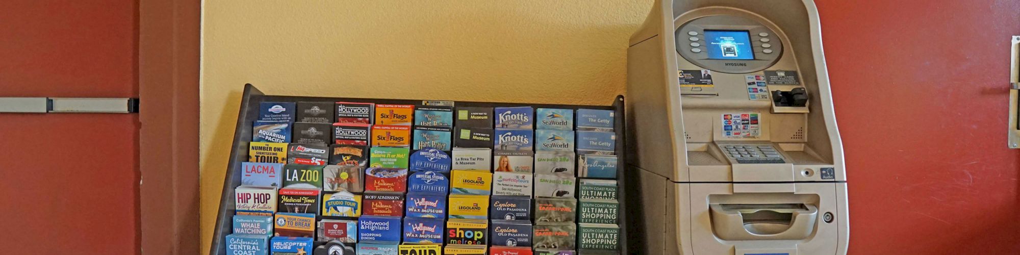 The image shows a display rack with brochures and an ATM next to a door labeled 104, against a yellow and red wall.