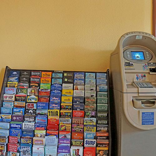 The image shows a brochure rack filled with various brochures next to an ATM in what appears to be a hallway.