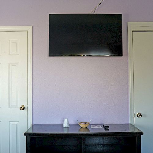 The image shows a wall with a mounted TV, two white doors, and a black dresser holding a cup, a remote, and a small bowl, with purple walls ending the sentence.