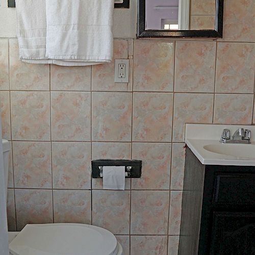 A small bathroom with a toilet, a sink, a towel hanging on a rack, and beige tiled walls. There's also a mirror above the sink.