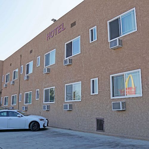 The image shows the side view of a motel building with multiple air conditioners and windows. A white car is parked in front of the motel.