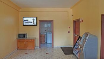 The image shows a room with yellow walls, a microwave on a counter, a TV, a door leading to a laundry area, and a vending machine.