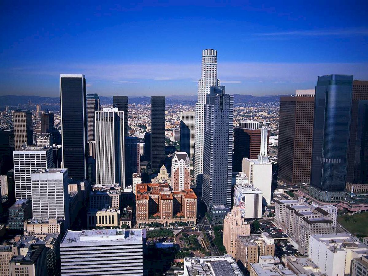 The image shows a cityscape with tall modern skyscrapers under a clear blue sky, likely depicting a downtown area.